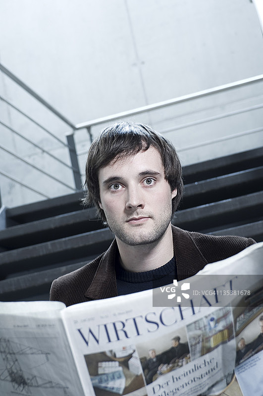 在楼梯上阅读报纸的年轻男人图片素材