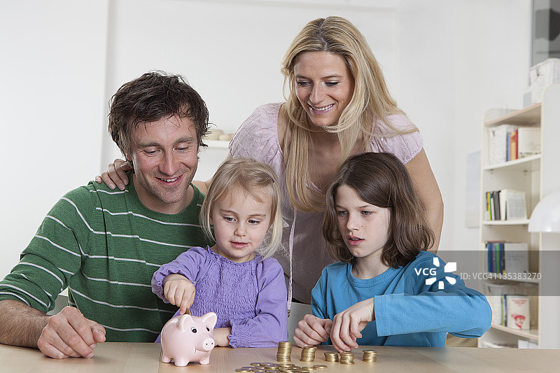 德国巴伐利亚慕尼黑，一家人拿着硬币和储蓄罐，面带微笑图片素材