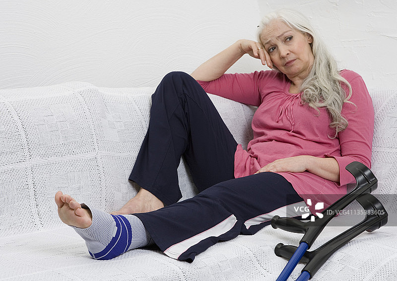 德国杜塞尔多夫：坐沙发上、拄着拐杖的缠绷带女子图片素材
