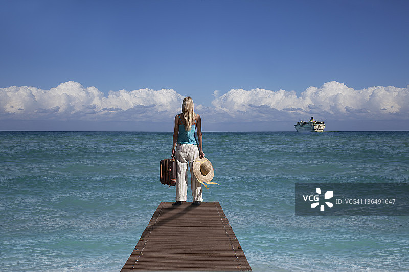带着行李箱的女人看着离开港口的船图片素材