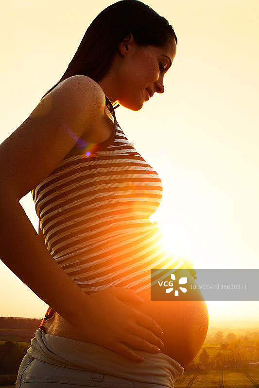 日落时分，孕妇托着隆起的肚子图片素材