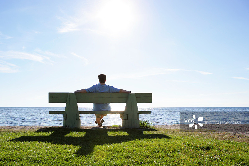 坐在公园长椅上俯瞰海洋的男士图片素材
