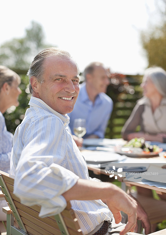 在露台餐桌上与朋友共进午餐的微笑男士肖像图片素材