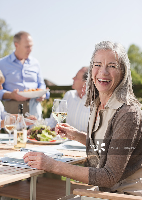 肖像微笑的年长妇女享受午餐与朋友在阳光餐桌图片素材