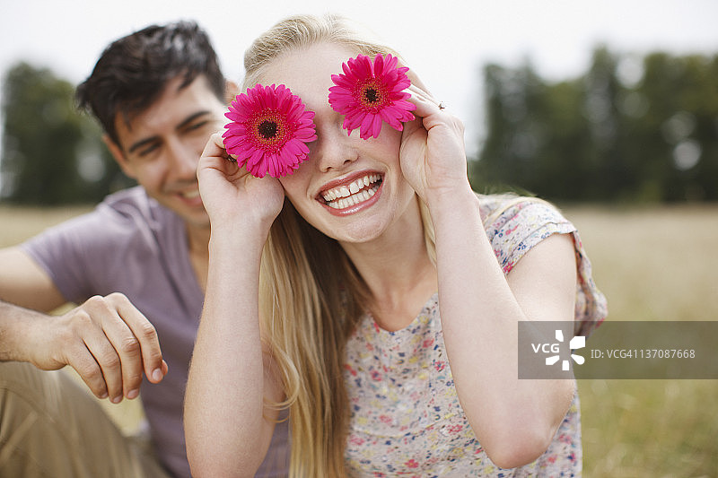 在乡村田野里用鲜花遮住眼睛的顽皮女人肖像图片素材