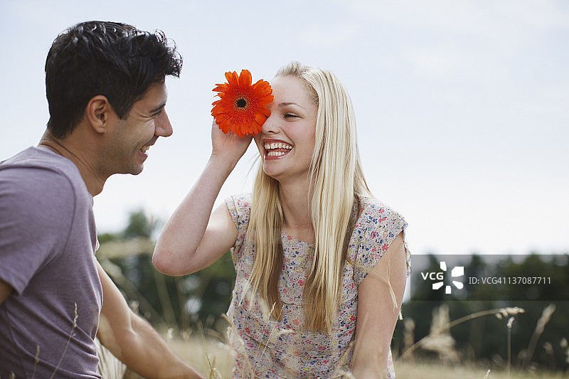 微笑的女人拿着花朵遮住眼睛，看着乡村田野里的男人图片素材