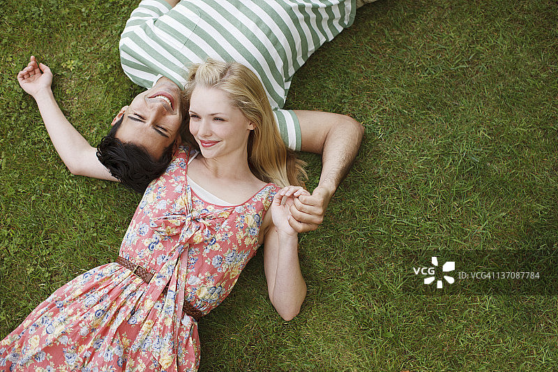 年轻情侣躺在草地上手牵着手图片素材