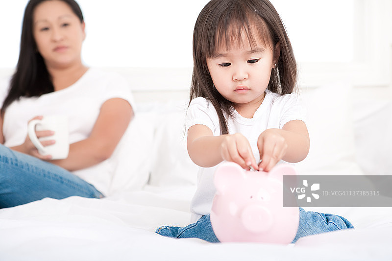 女孩往小猪存钱罐里放钱图片素材