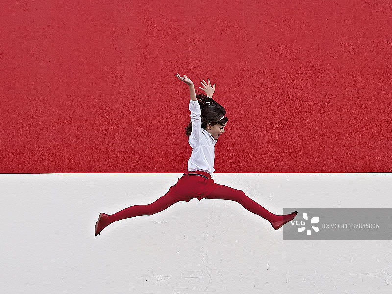 女孩在红墙边跳跃图片素材