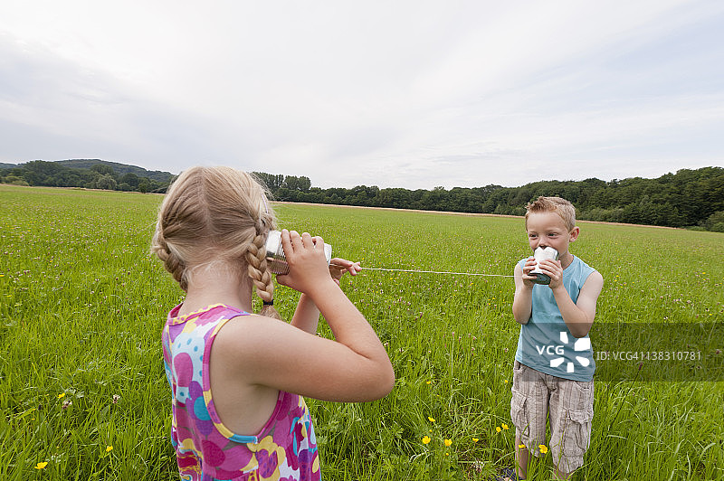 德国北莱茵-威斯特法伦亨内夫：在草地上玩听筒电话的男孩和女孩图片素材