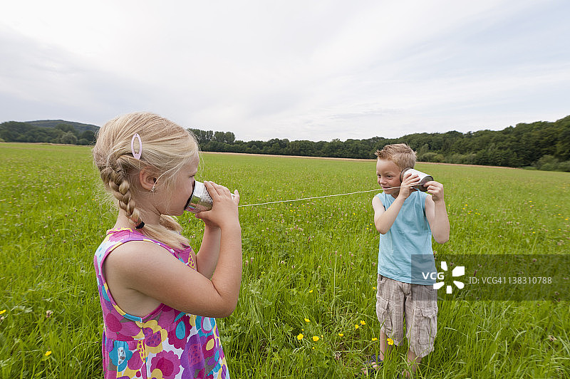 德国北莱茵-威斯特法伦亨内夫：在草地上玩听筒电话的男孩和女孩图片素材