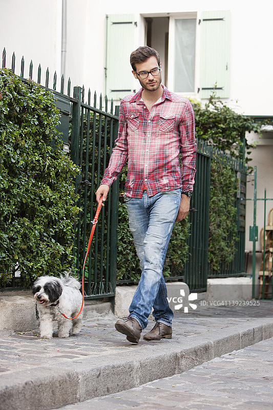 男人在法国法兰西岛巴黎的人行道上牵着狗图片素材