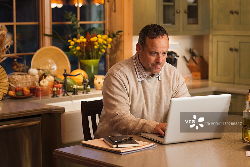 在厨房用笔记本电脑工作的年长男性图片素材