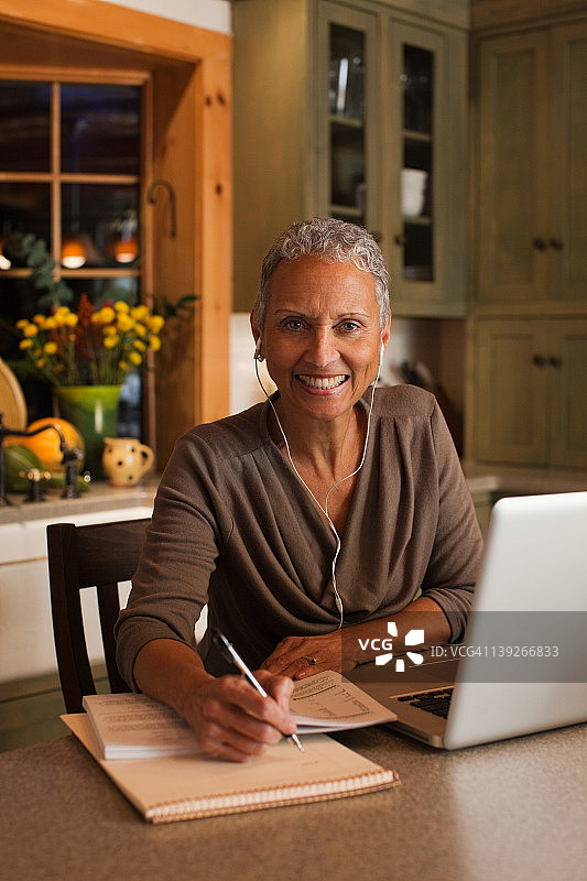中年妇女使用笔记本电脑并佩戴耳机图片素材