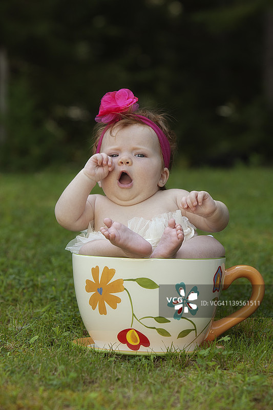 坐在大茶杯里打哈欠的女婴图片素材