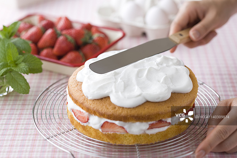 手在海绵蛋糕上涂抹奶油图片素材