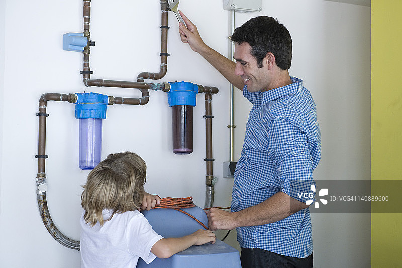 男孩看着父亲修理家用滤水系统图片素材