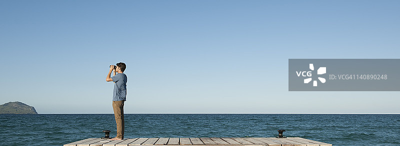 男人站在码头上用双筒望远镜观看海景，侧视图图片素材