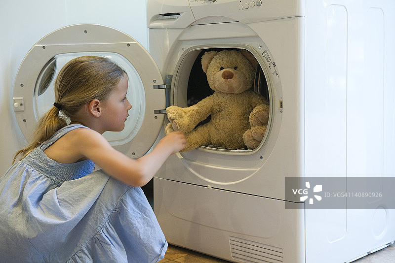 小女孩从烘干机里拿出泰迪熊图片素材