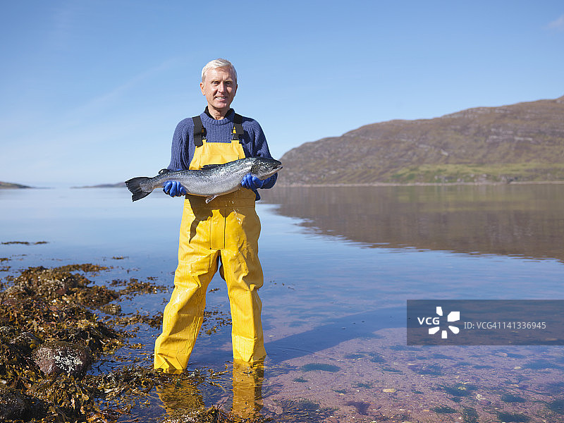 站在湖中手持刚捕获的三文鱼的渔夫肖像图片素材