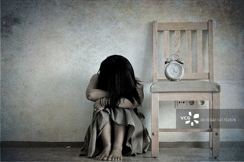 悲伤的女孩低着头，双手抱膝图片素材
