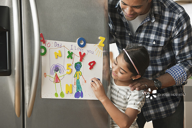 父亲看着冰箱上女儿的画作图片素材