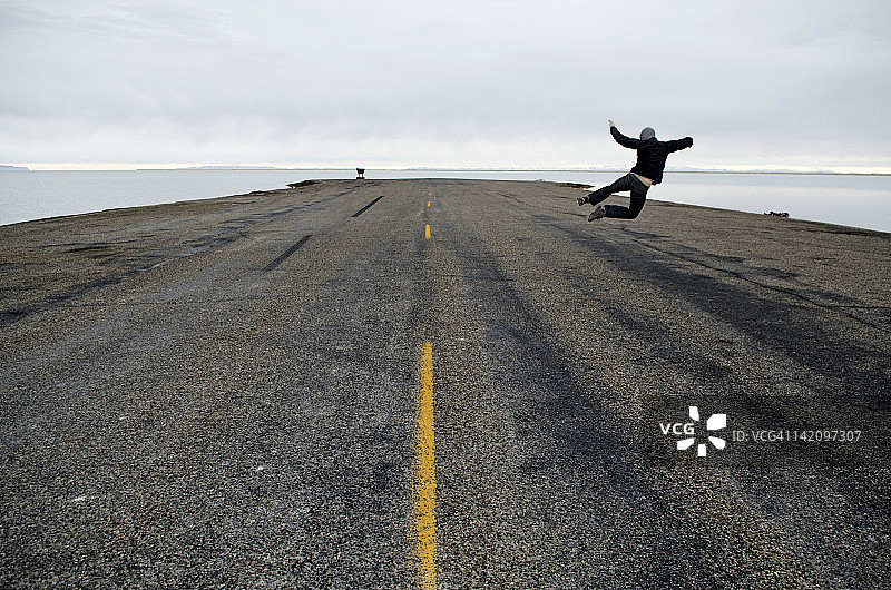男人在道路尽头和犹他州邦纳维尔盐滩起点跳跃图片素材