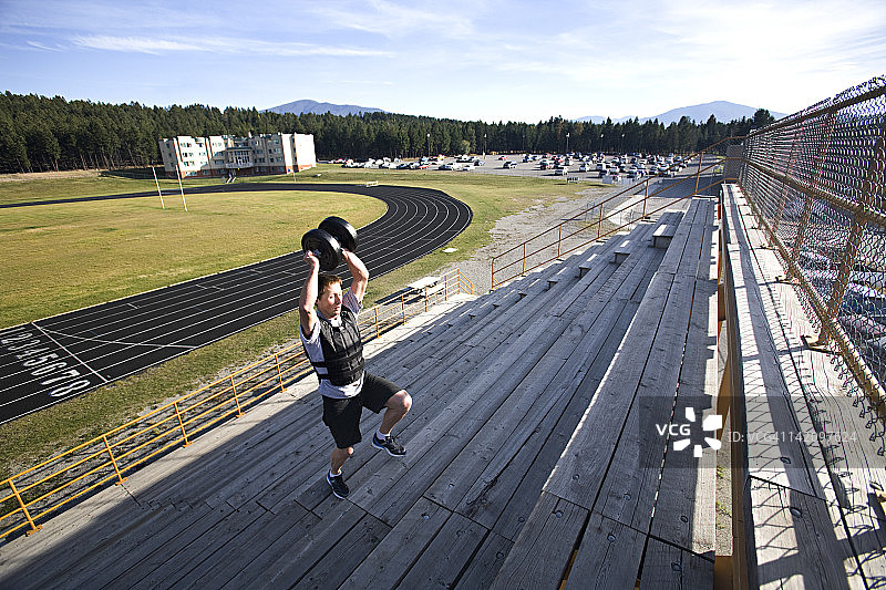 穿着短裤、跑步上楼梯、举着负重背心和重物的男子图片素材