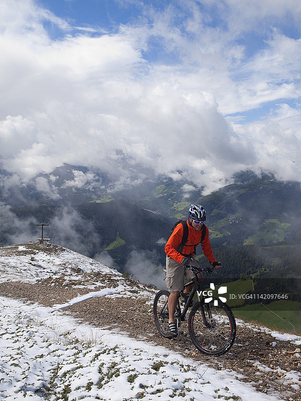 山地自行车手到达克龙普拉茨山顶，背景是群山、十字架和云彩图片素材