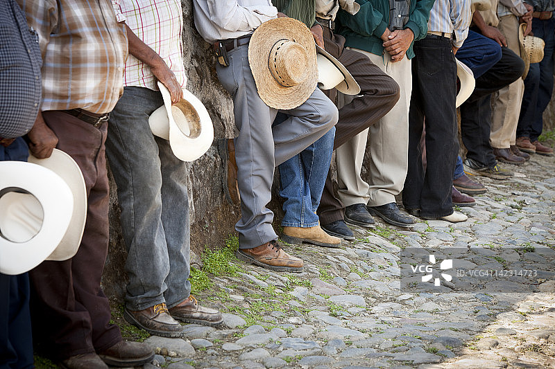 戴着帽子和靴子的墨西哥男人靠墙站立图片素材