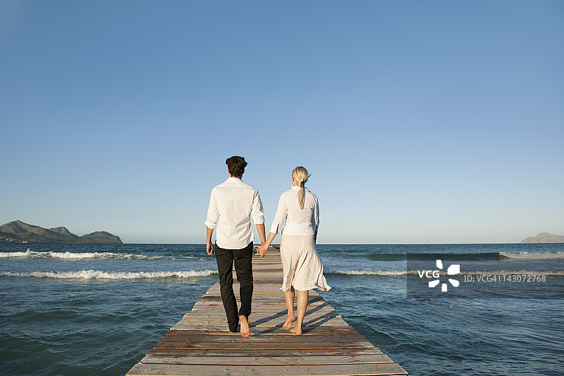 情侣在码头上牵手散步，后视图图片素材
