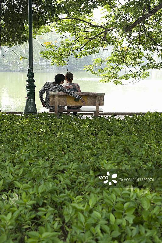 情侣坐在越南河内湖边的长椅上图片素材