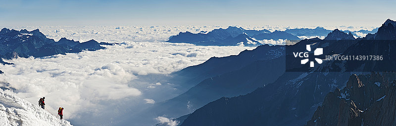 登山者攀登云层之上的高海拔山脊图片素材