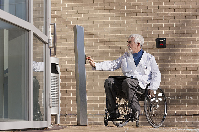 在医院入口处，坐在轮椅上的肌肉萎缩症患者按下无障碍门的按钮图片素材