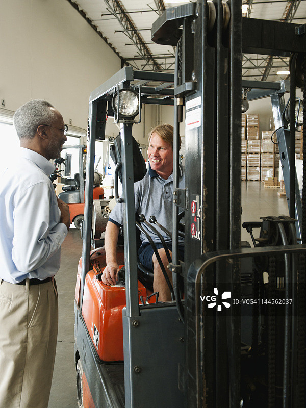 美国加利福尼亚州圣安娜，商人和叉车司机在仓库交谈图片素材
