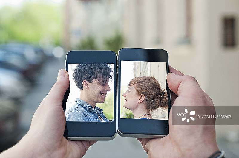 年轻情侣通过两部智能手机交流图片素材