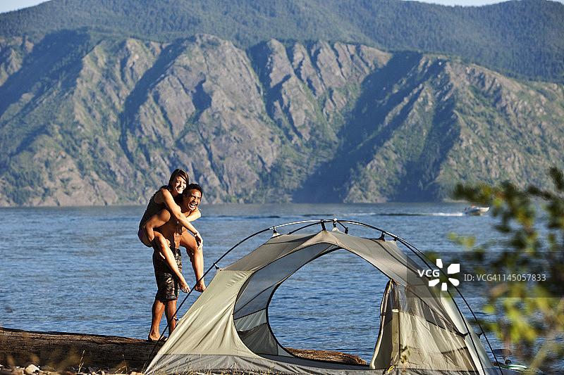 快乐的年轻夫妇在爱达荷州湖边的露营之旅中微笑和大笑图片素材