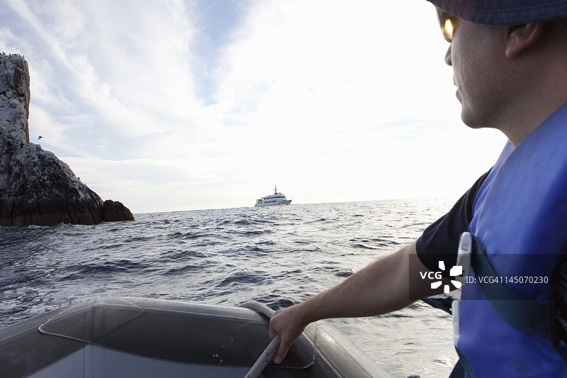 男子驾驶充气船驶向一艘船图片素材