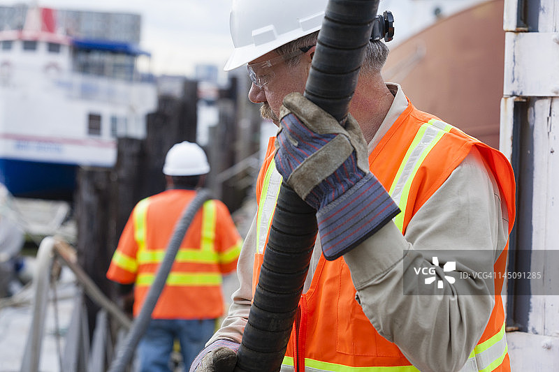 环境工程师将石油软管延伸至商船，清理有毒废物图片素材