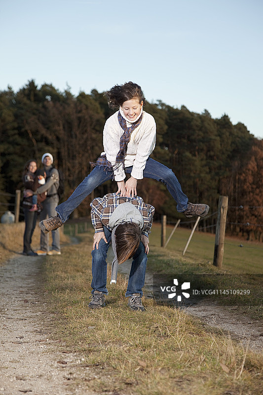 德国巴伐利亚儿童玩跳山羊游戏，父母站在背景中图片素材