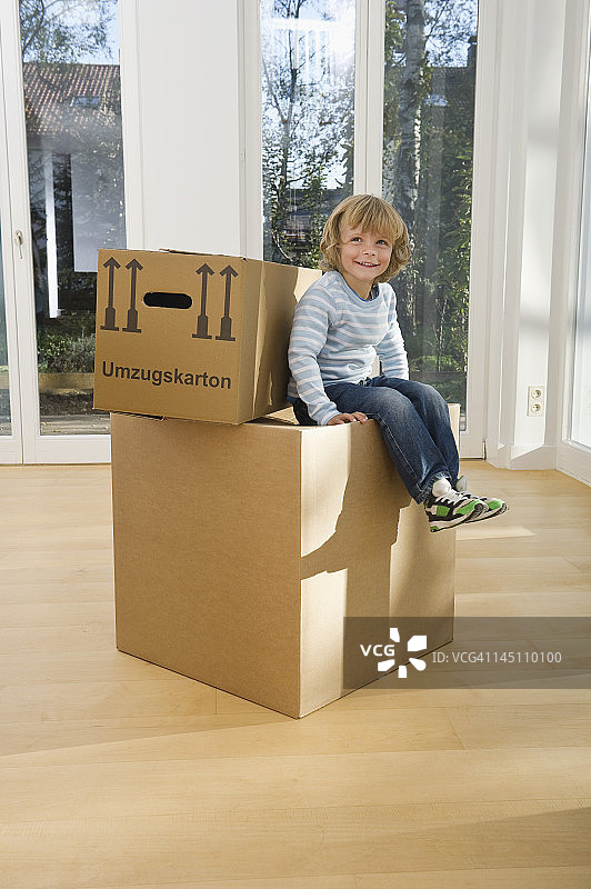 德国巴伐利亚格罗本策尔，男孩坐在纸板箱上微笑图片素材