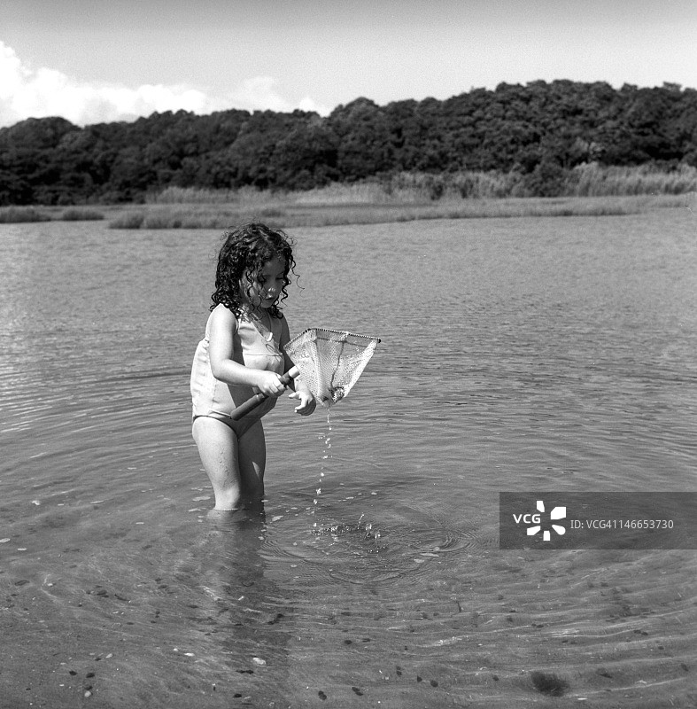 穿着泳衣，用渔网捕鱼的年轻女孩图片素材