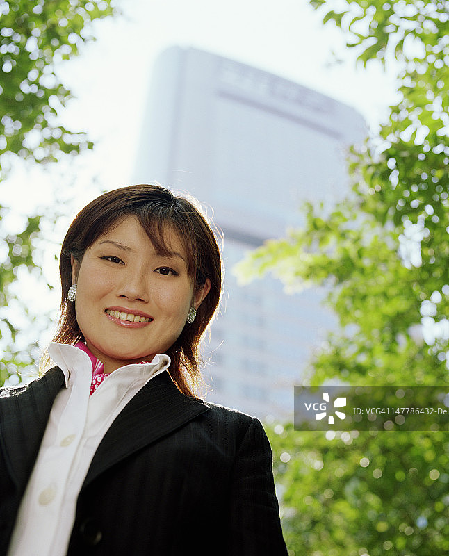 年轻女子微笑，高楼背景，低角度人像图片素材