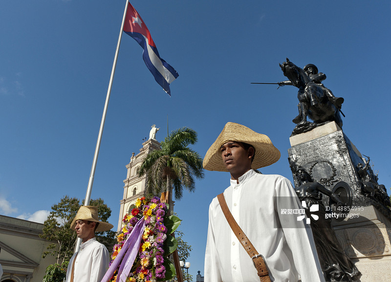 身着礼服的士兵在中央公园的雕像鲜花旁等待，上方悬挂着古巴国旗图片素材