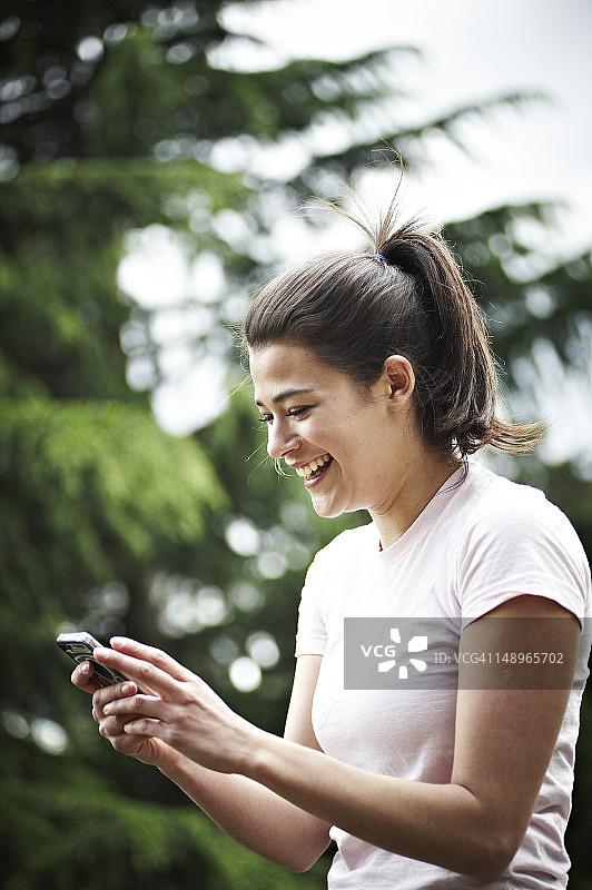 在公园里用手机微笑的女子图片素材