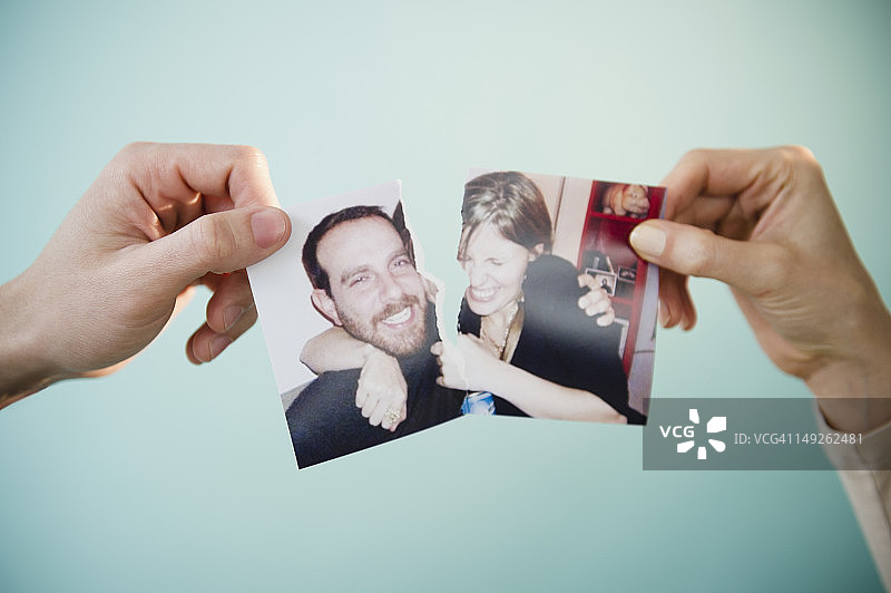 男女双手拿着撕毁的合影照片，工作室拍摄特写图片素材