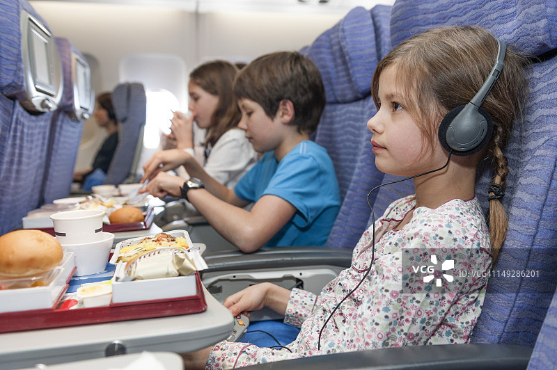 女孩在飞机上看电影，餐盘上放着航空餐图片素材