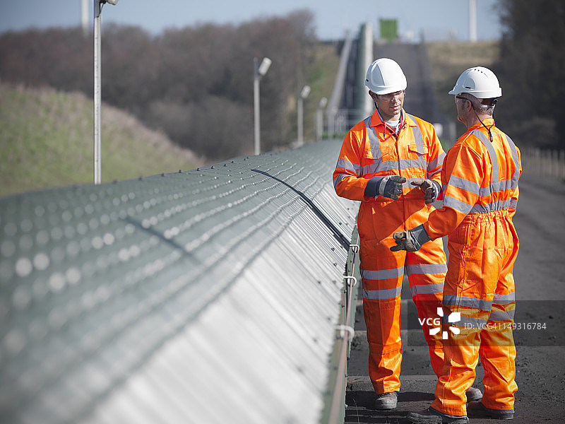 露天煤矿中，煤矿工人在传送带旁讨论图片素材