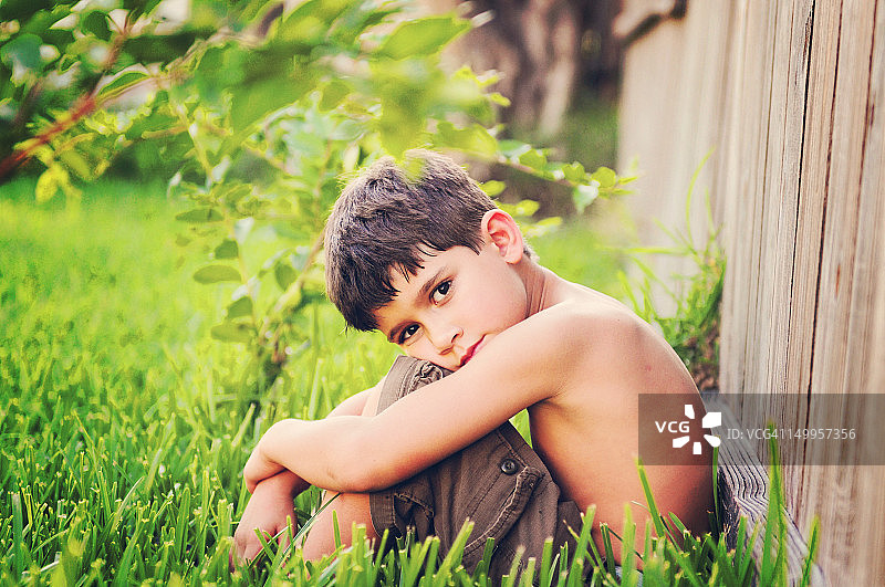 男孩坐在灌木丛下的草地上图片素材