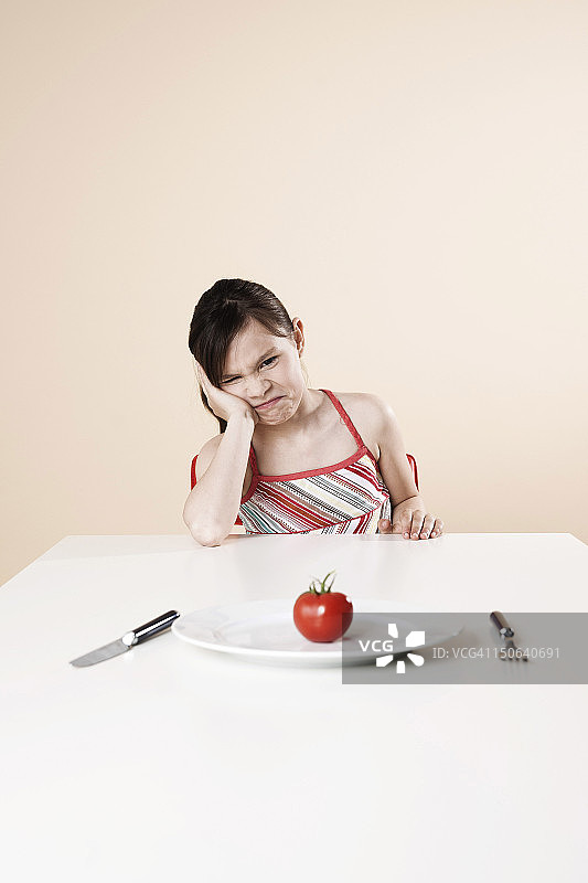 生闷气，坐在桌旁吃番茄的女孩图片素材
